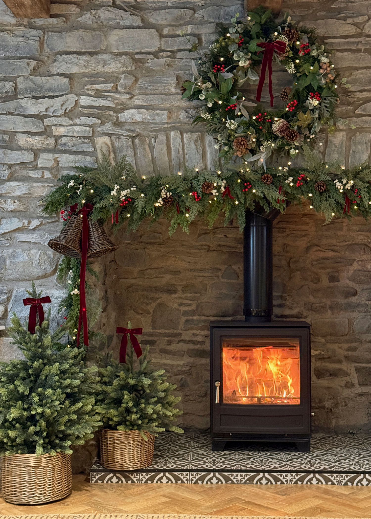Festive hearth with a roaring fire, wicker tree planters and a traditional garland draped across a rustic stone fireplace.