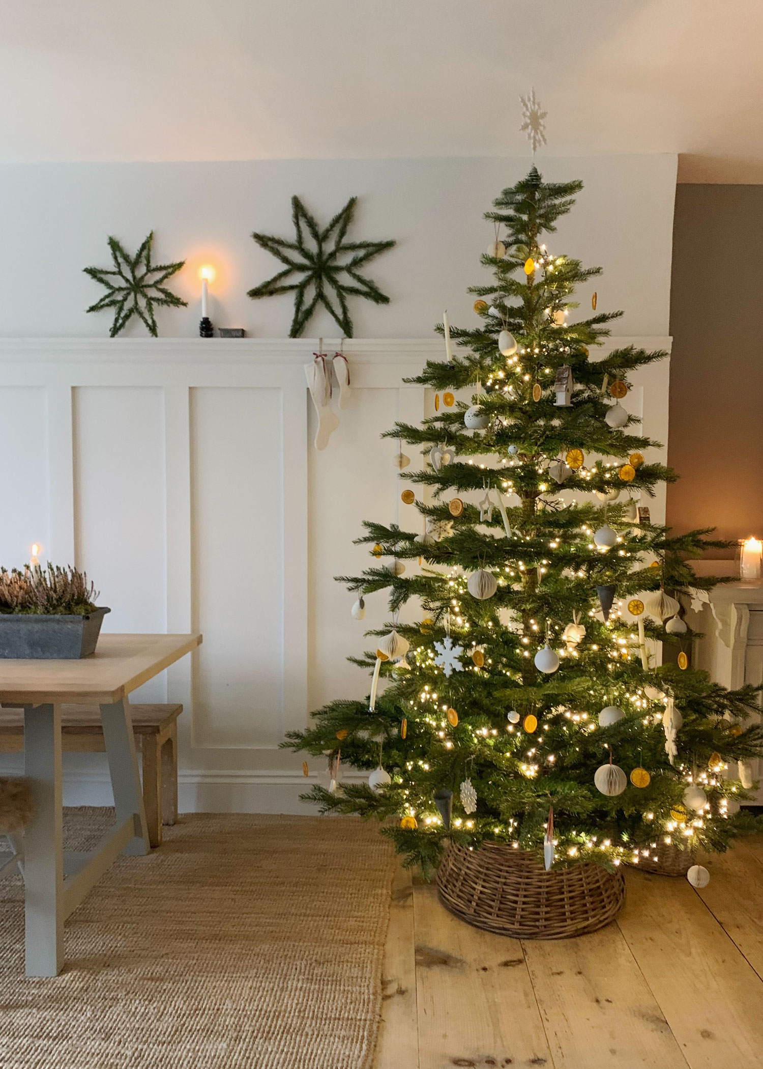 Scandi-style Christmas tree with gold and white ornaments, styled in a rustic wicker tree skirt on natural wooden floors.