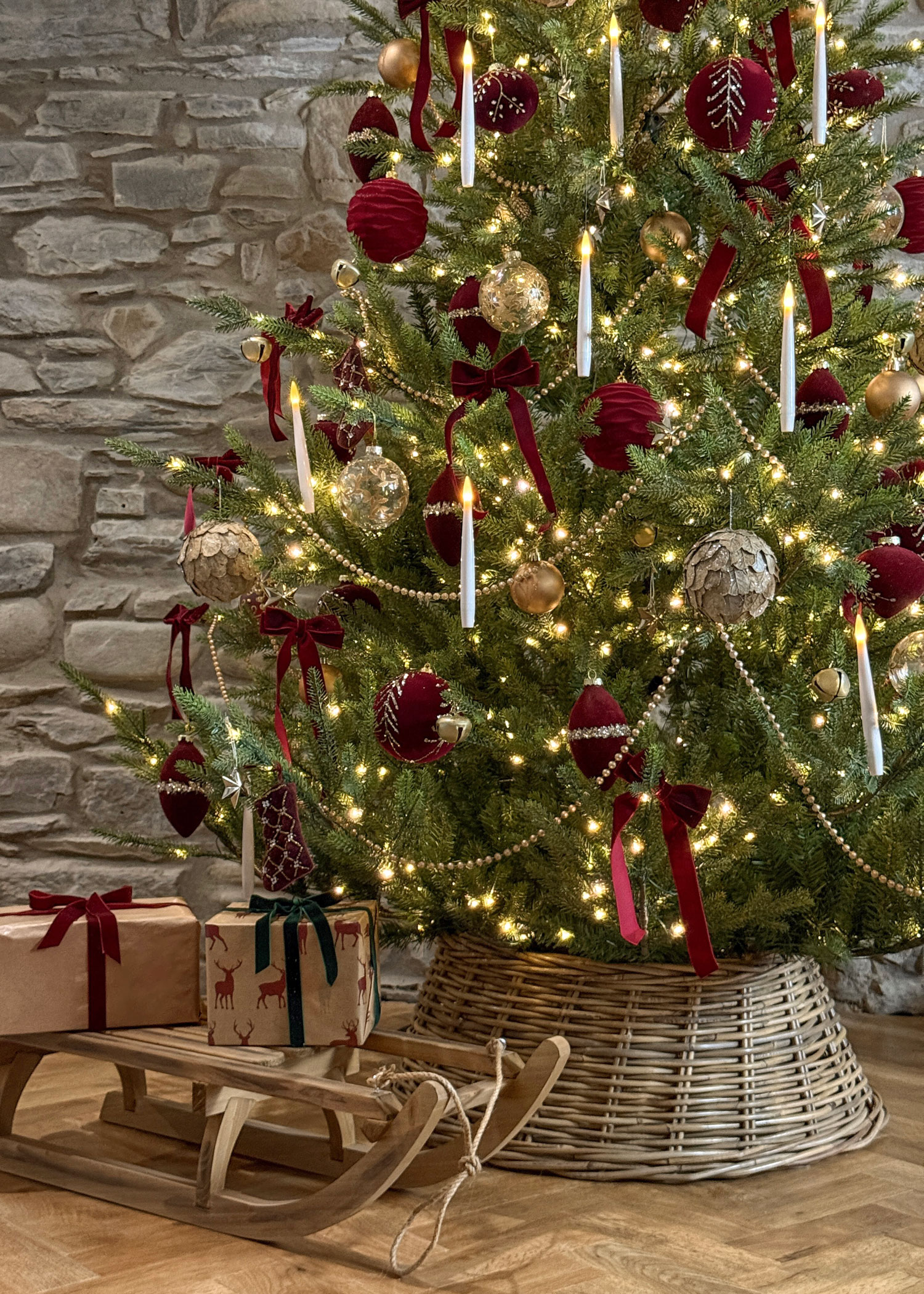 Close-up of a Christmas tree with gold and red decorations, styled in a natural wicker tree skirt beside a wooden sleigh.