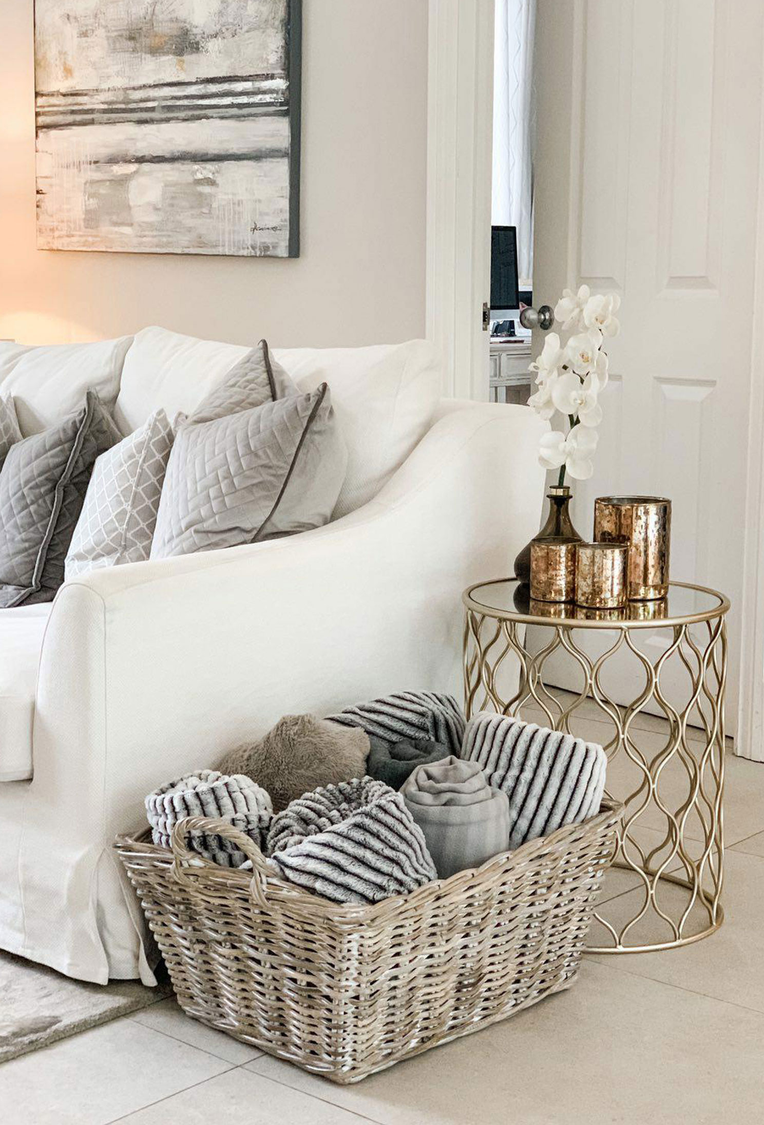 Cosy neutral living room with a wicker blanket basket beside a white sofa, neatly filled with rolled throws and textured cushions.