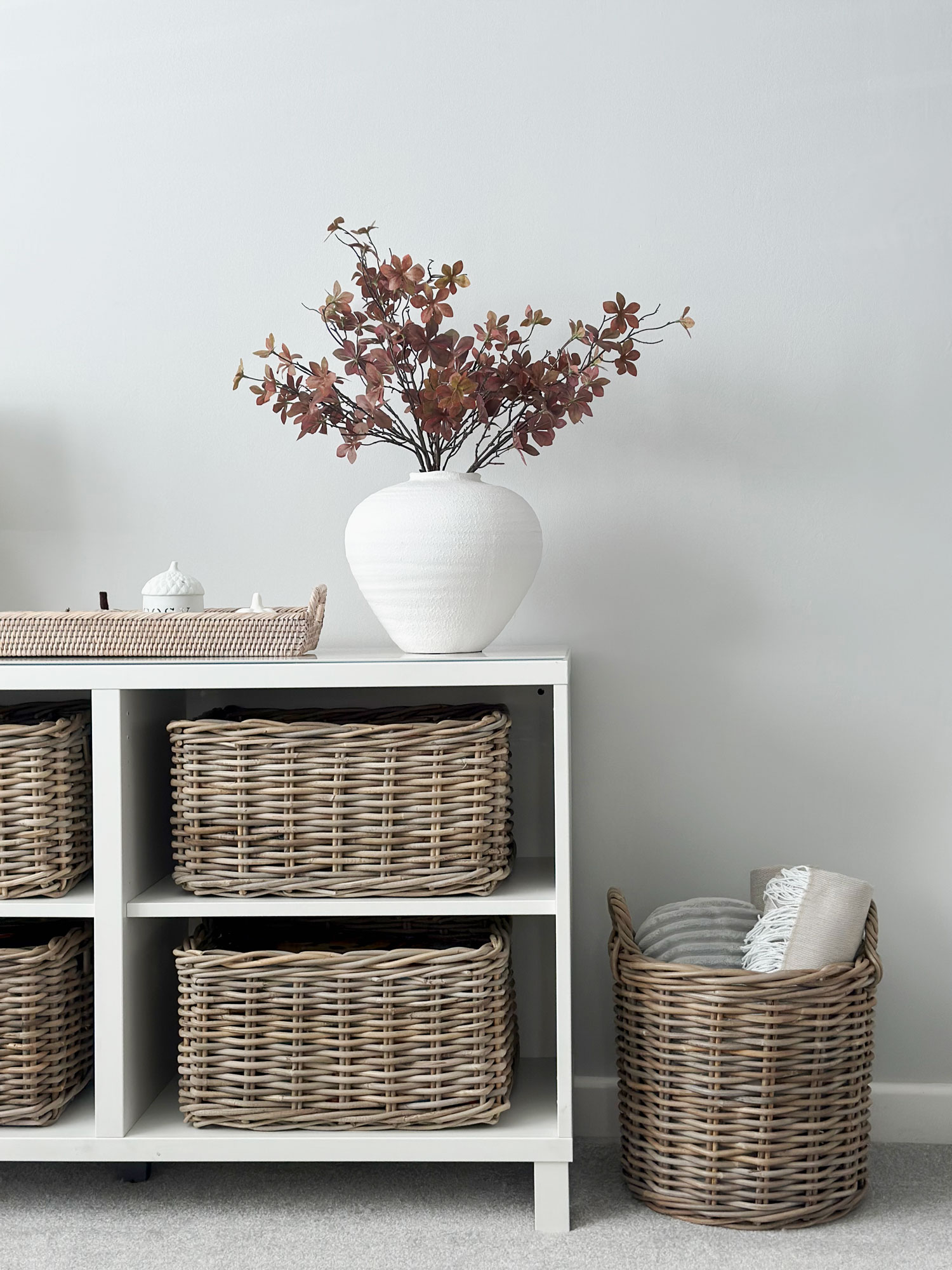 Stylish storage unit with rattan baskets and a round blanket basket on the side, ideal for keeping soft furnishings close to hand.