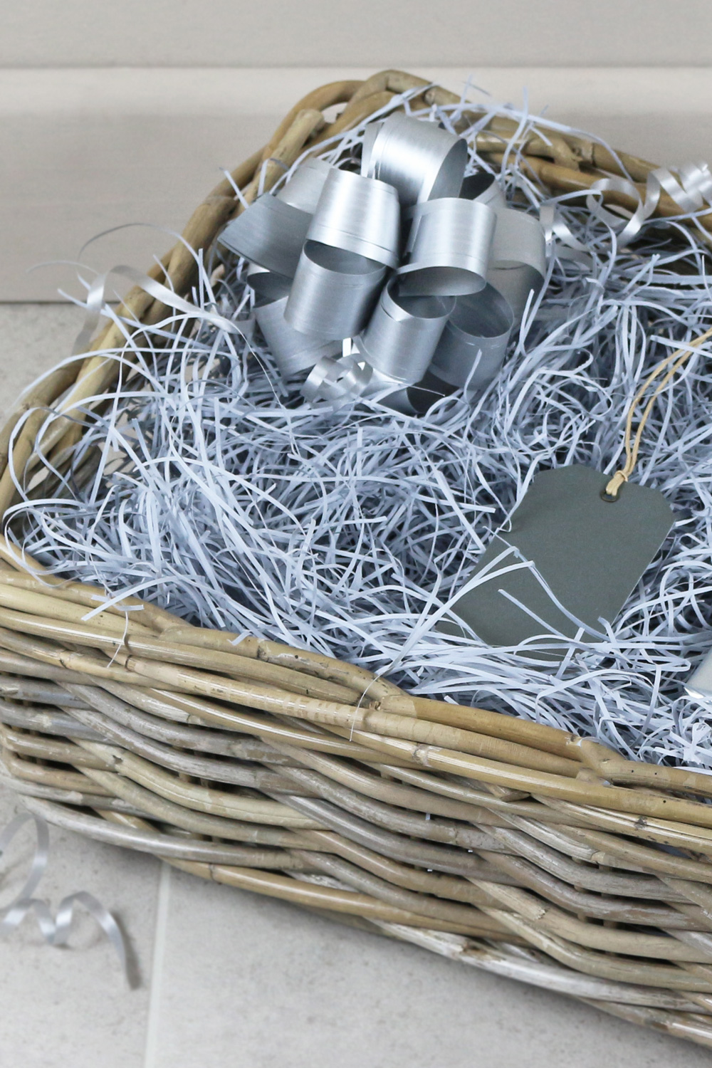 a grey and buff wicker basket with silver shred, bow and tag. 