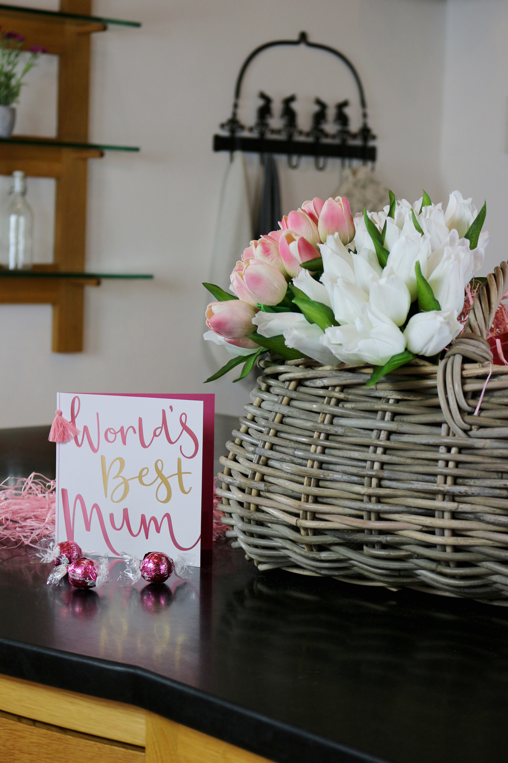 a 'worlds best Mum' card next to a bunch of flowers displayed in a wicker basket
