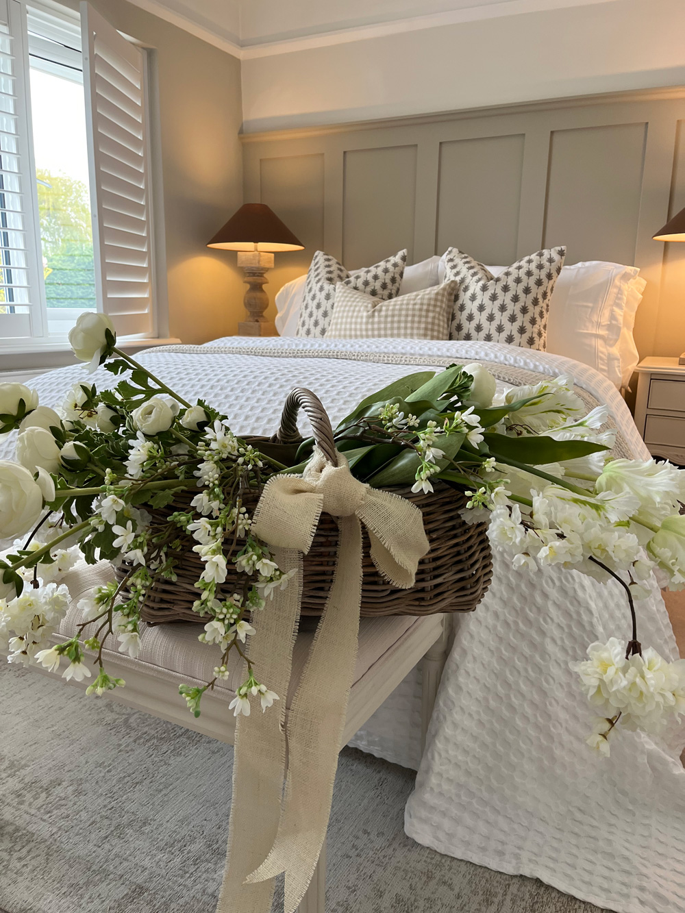 A stunning fresh bedroom styled with a fresh bouquet of flowers on the bed in a rattan shopping basket.