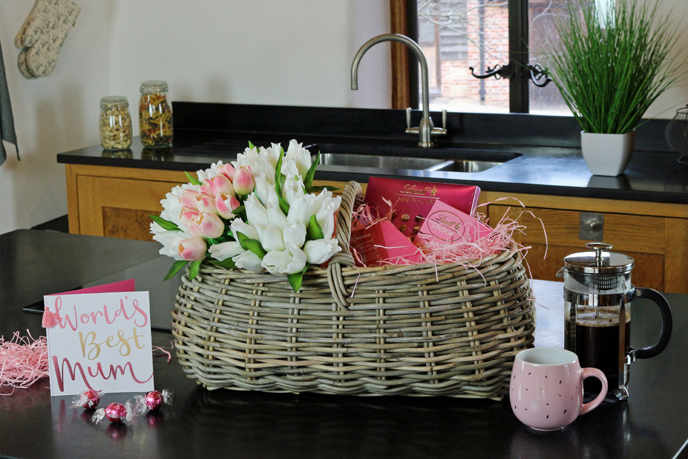 a beautiful mother's day trug basket filled with fresh flowers and chocolates in a kitchen setting