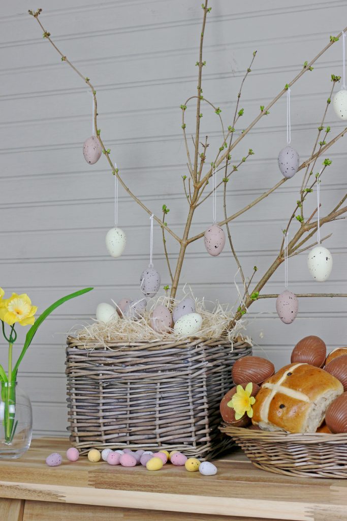 An indoor wicker plant pot complete with hot cross buns and decorative eggs.