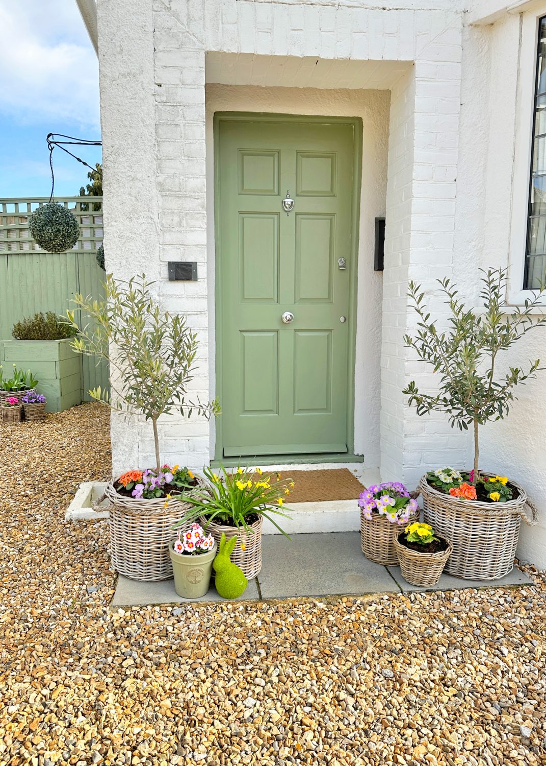A front door decorated for spring time, complete with rattan plant pots with seasonal flowers