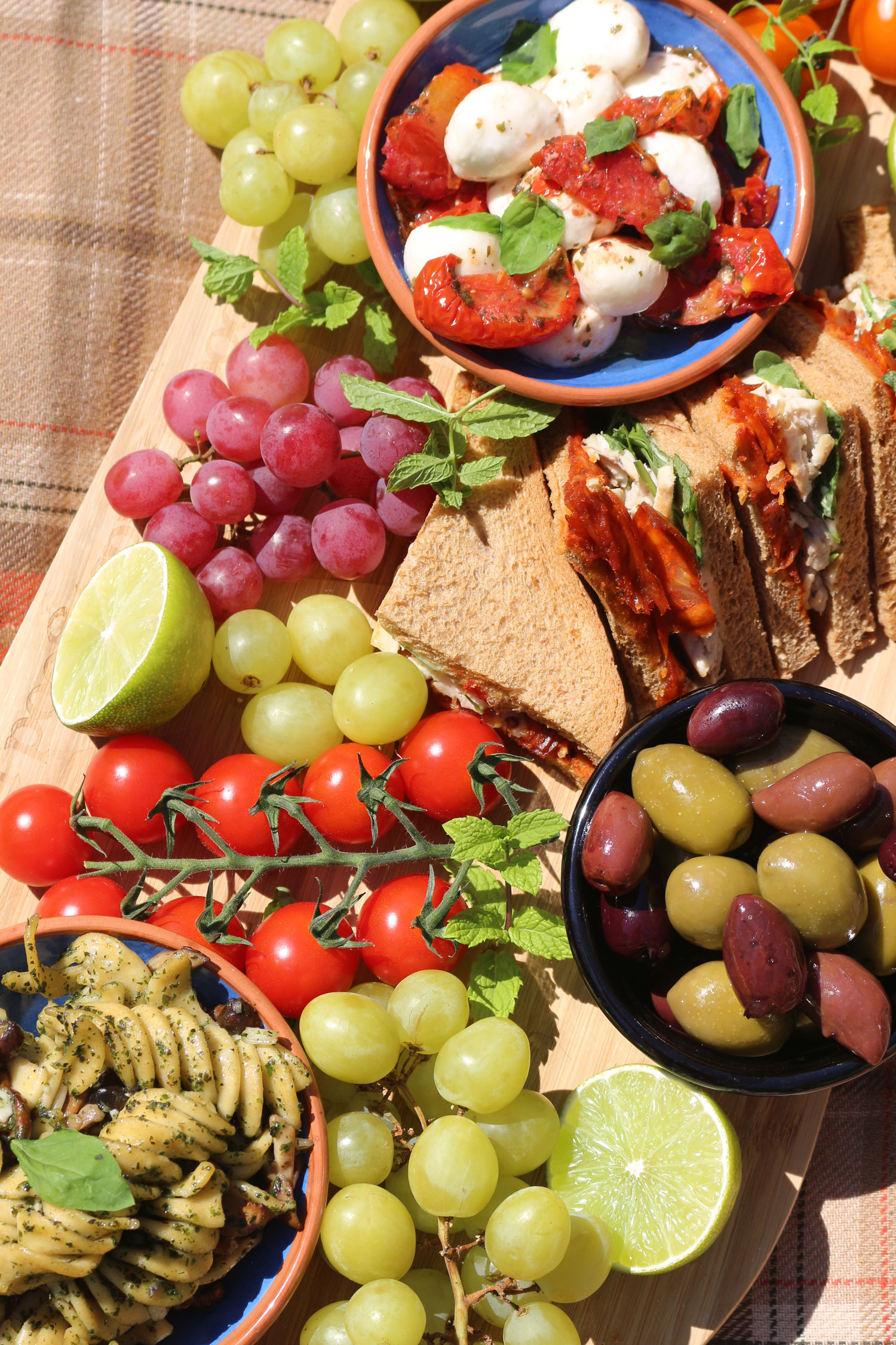 A selection of indulgent picnic food including pasta, olives, mozzarella and sandwiches.
