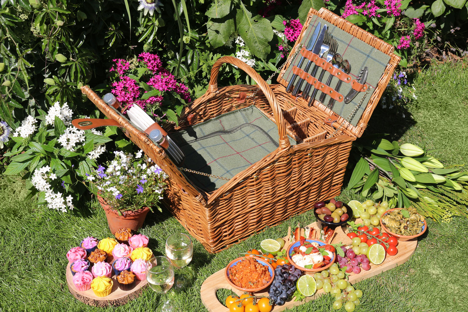 A stylish green tweed picnic hamper with a double lid, filled with an assortment of delectable food.