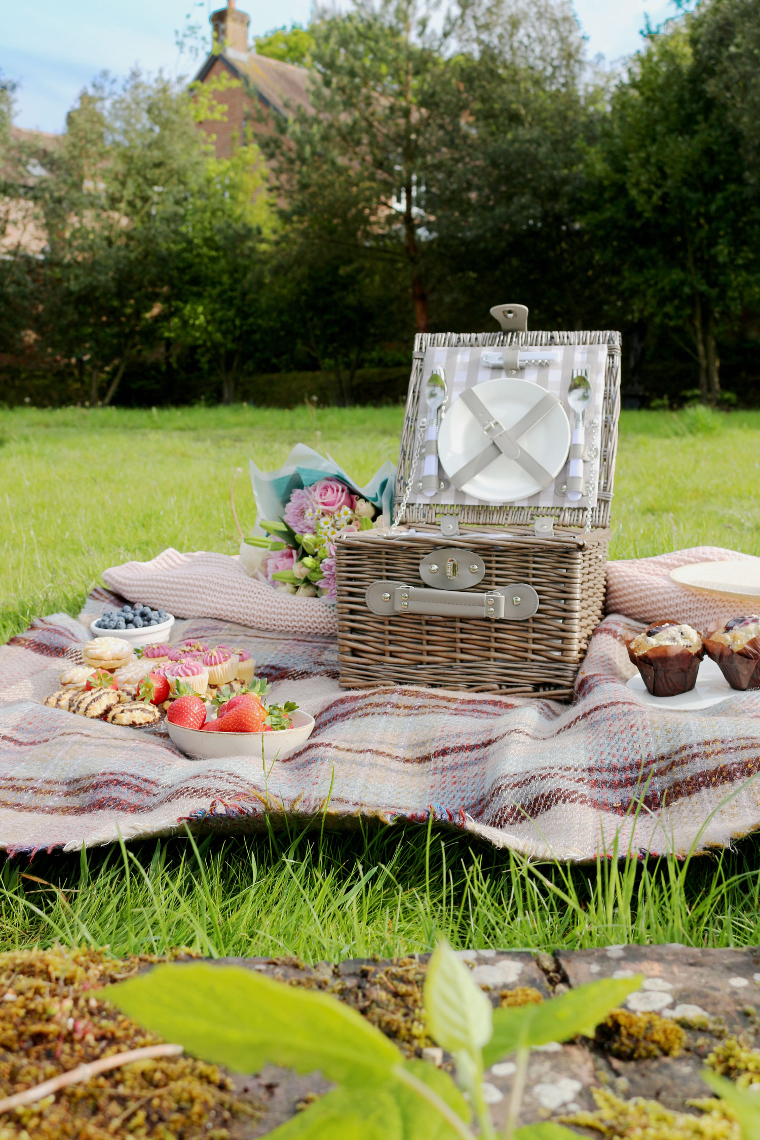 A grey wicker picnic basket with a selection of scrumptious food