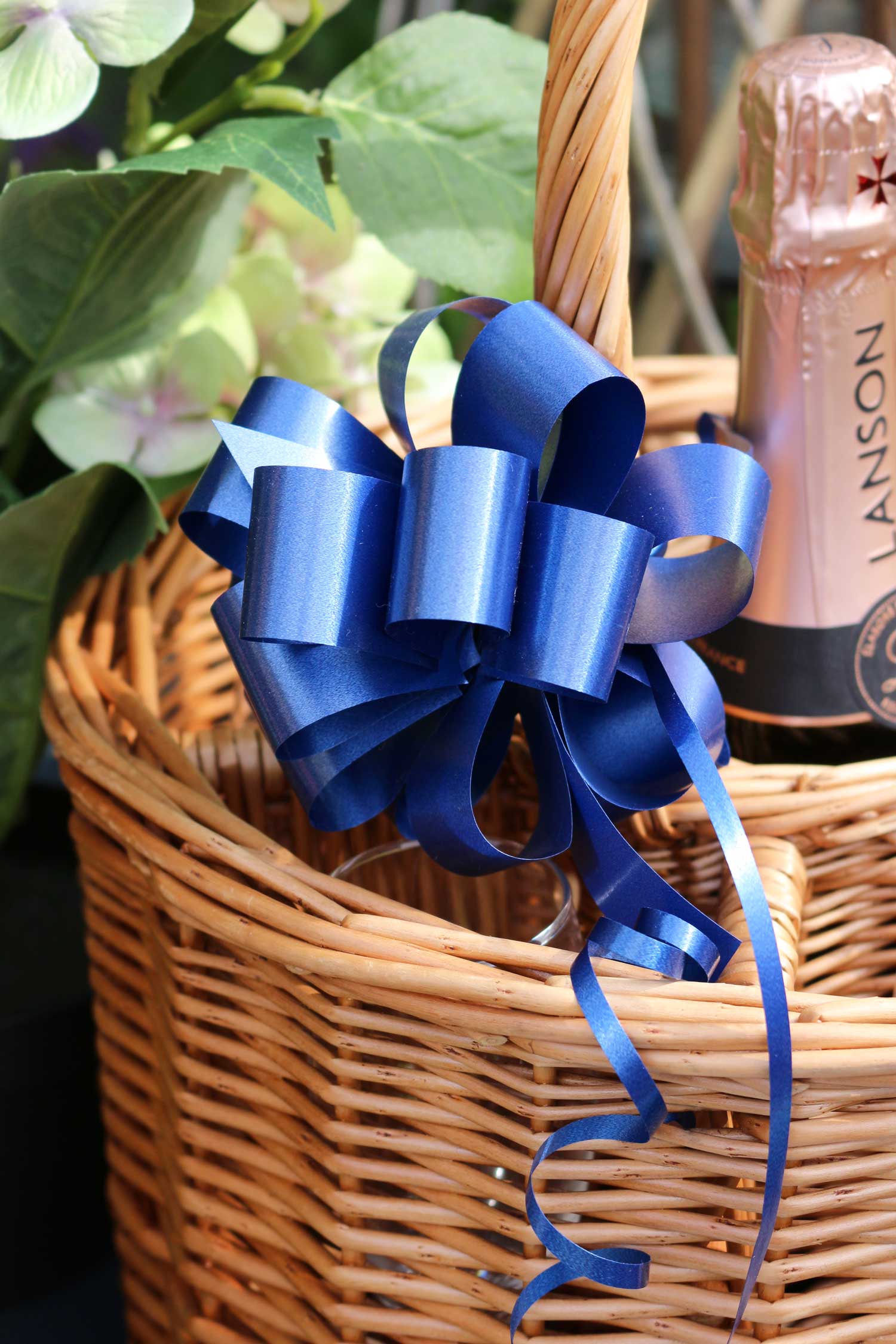 A navy blue gift bow attached to a wicker wine basket