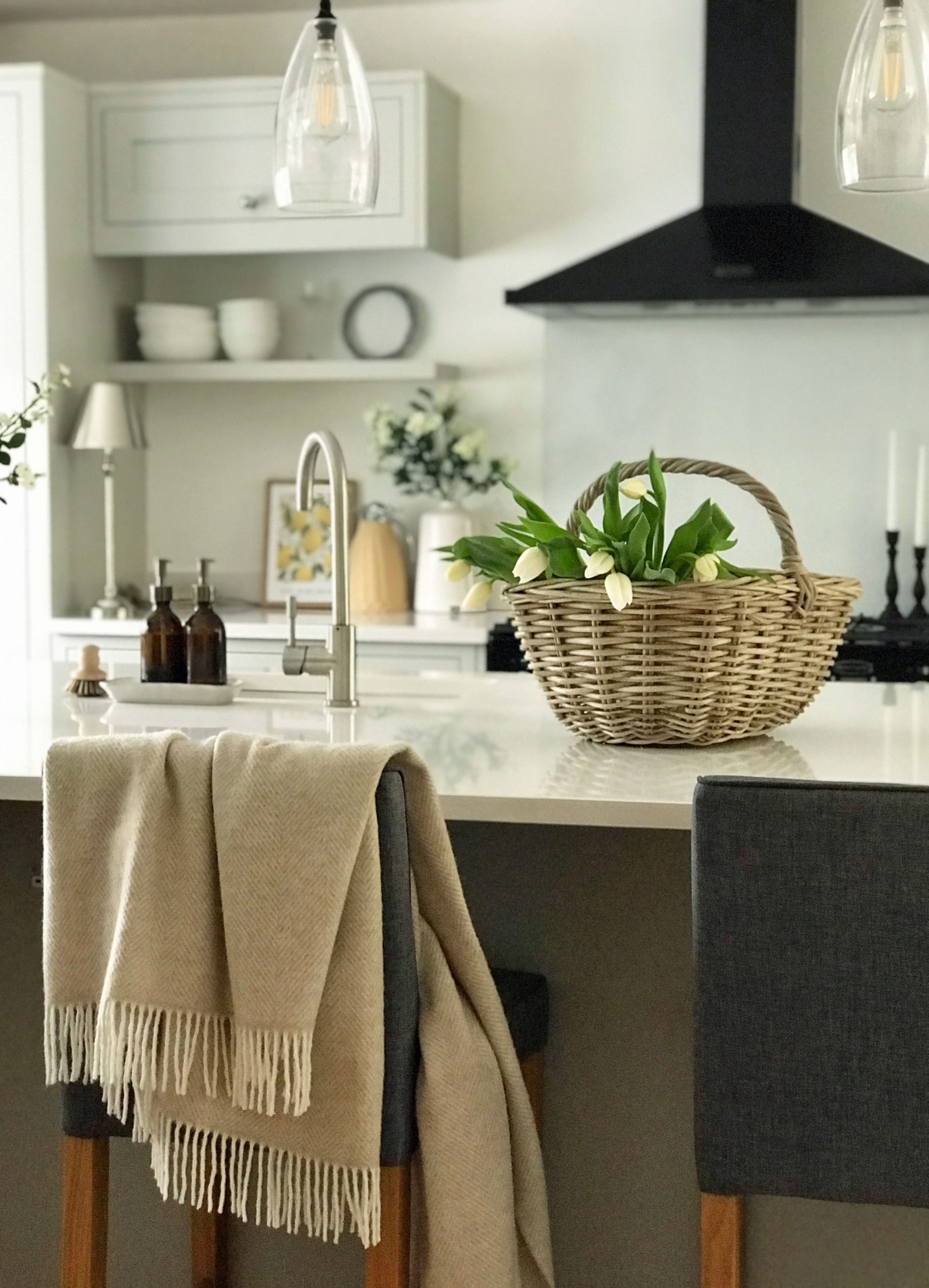 Wicker trug basket filled with white tulips styled on a glossy kitchen island in a modern neutral home