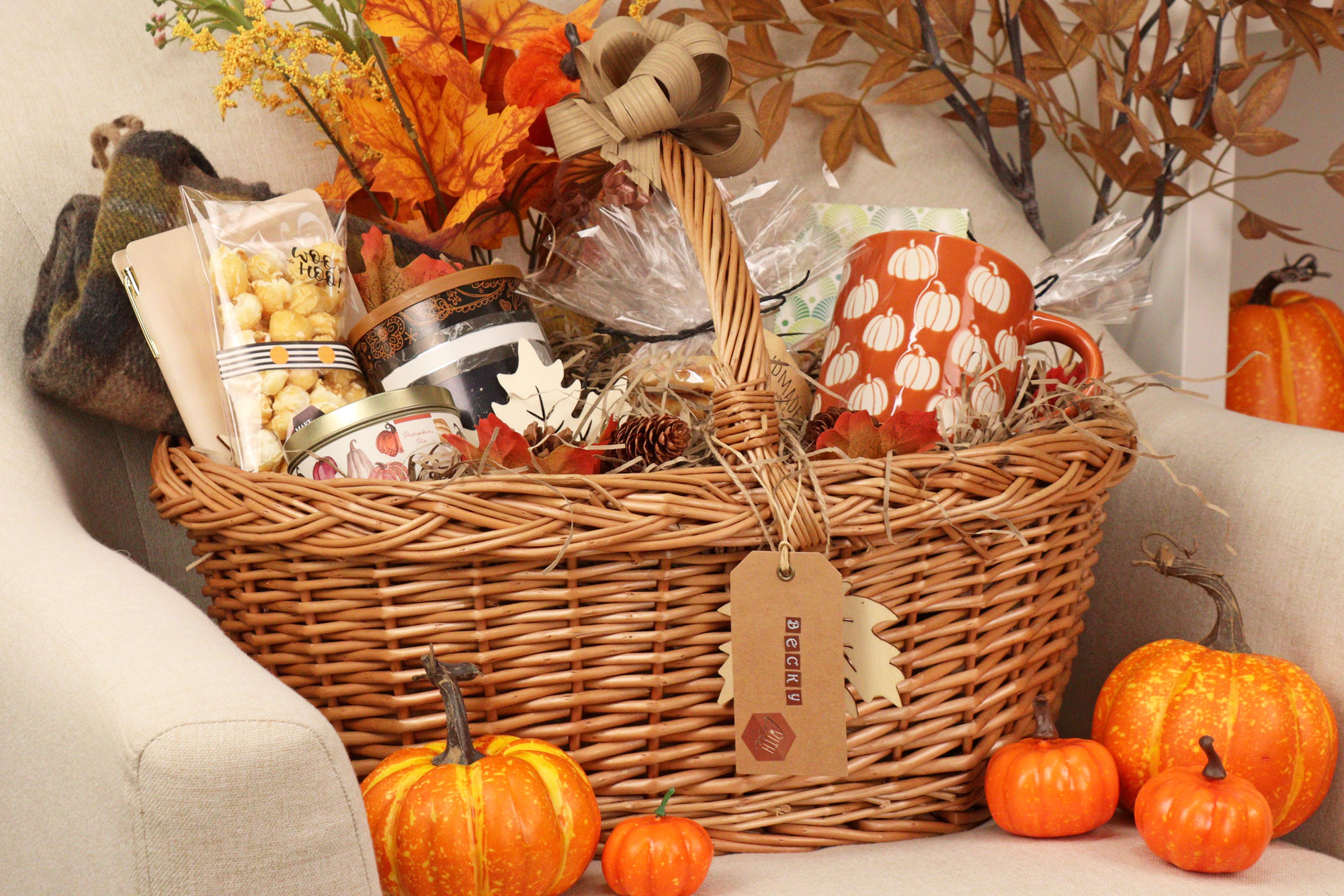 Large wicker Boo Basket filled with autumn treats, pumpkin-themed mug, scented candles, caramel popcorn, and orange foliage décor.