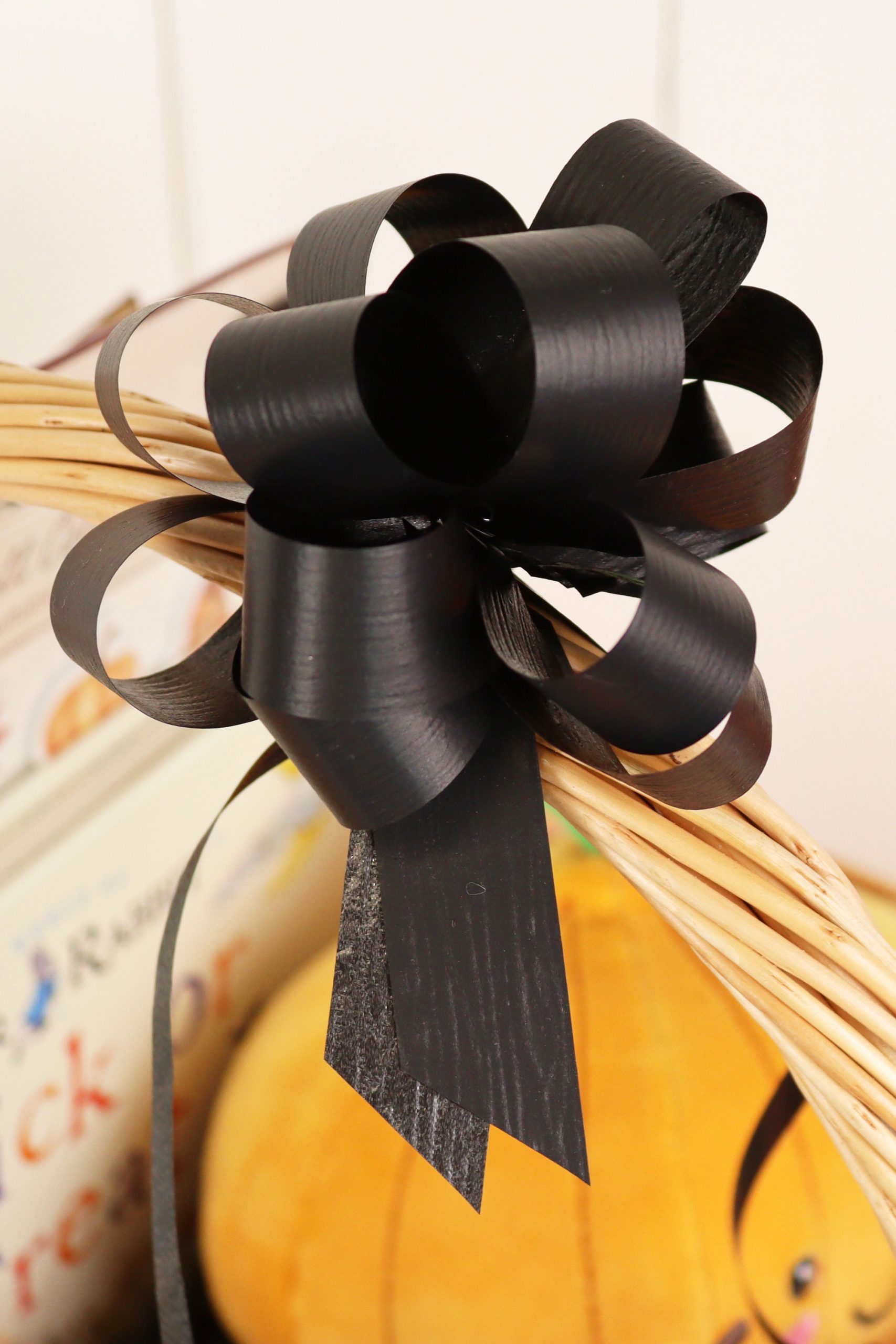 A luxurious black gift bow, displayed on the handle of a wicker hamper basket.