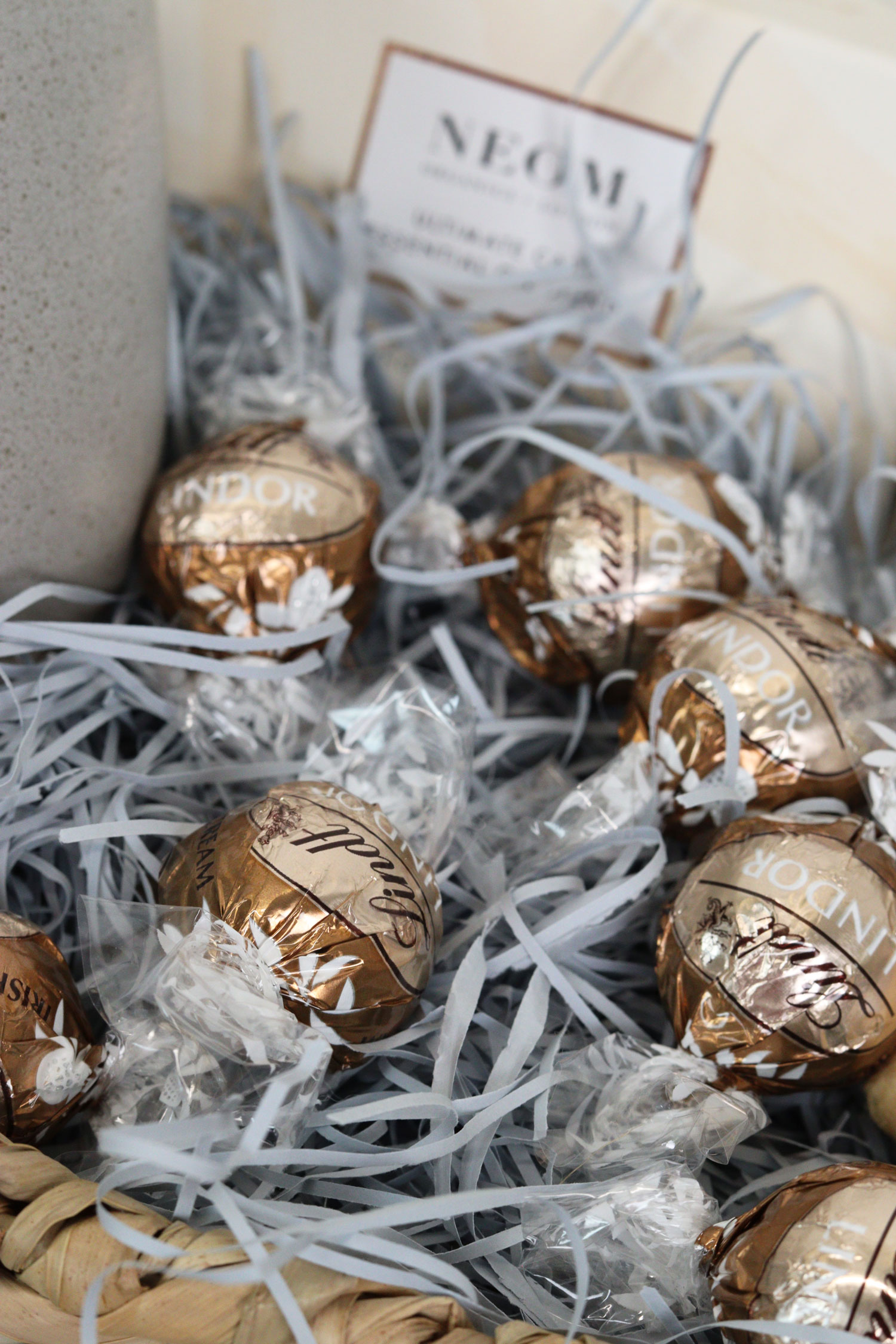 Lindor milk chocolate truffles resting in a burr basket with shredded paper and a wellbeing card in the background.