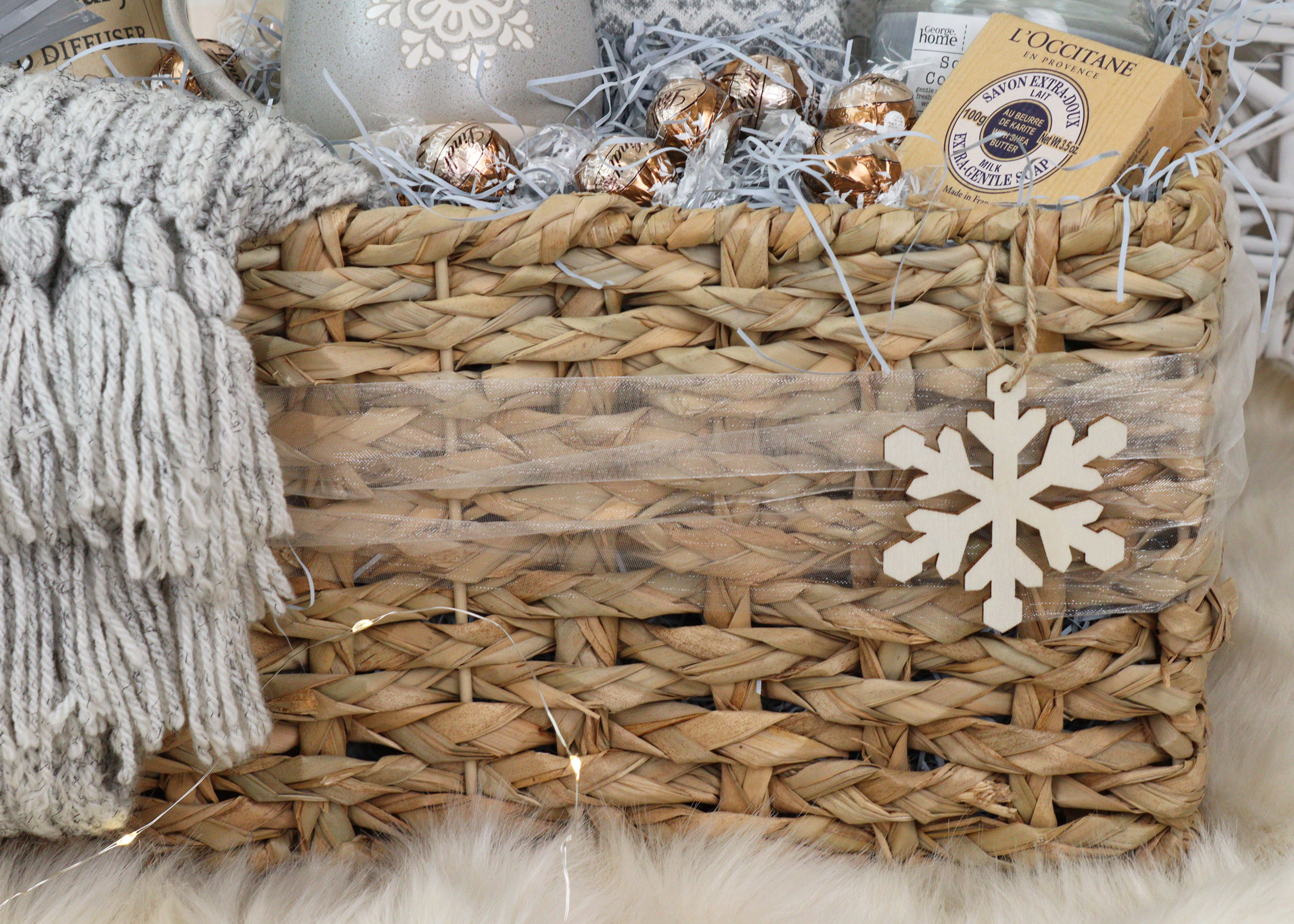 Front view of a burr basket filled with winter gifts, wrapped in soft netting and finished with a wooden snowflake tag.