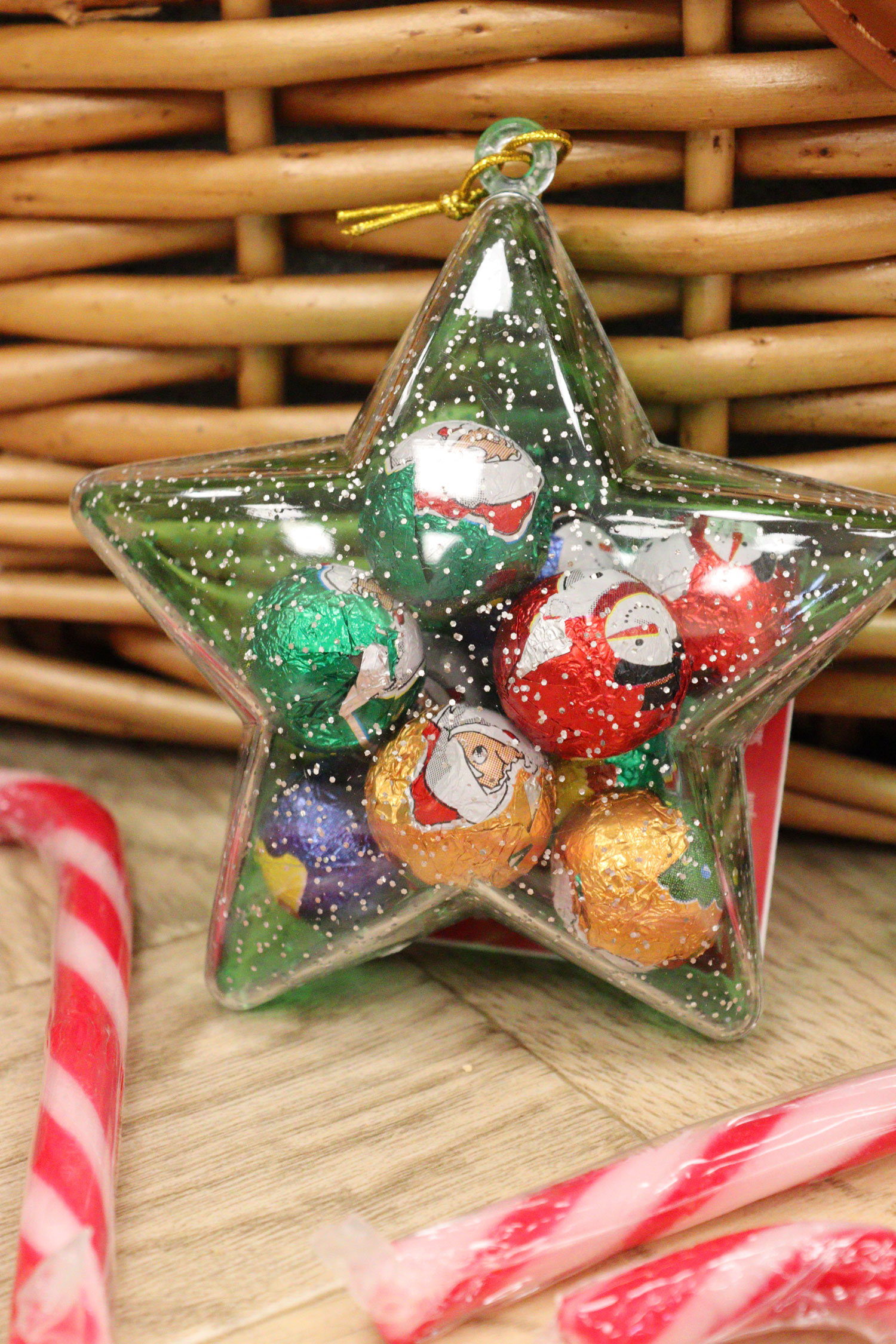 Clear star-shaped Christmas bauble filled with foil-wrapped Santa chocolates, next to striped candy canes.