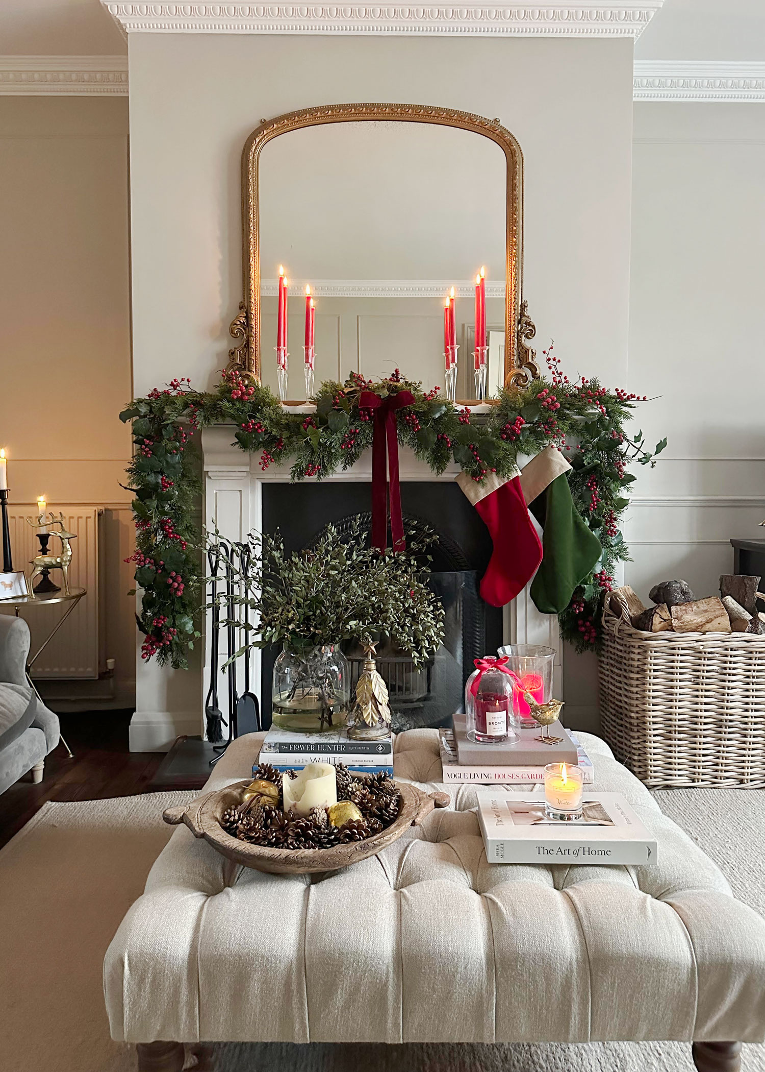 Festive fireplace styled with stockings, red candles, and a large wicker log basket filled with firewood for a cosy Christmas feel.