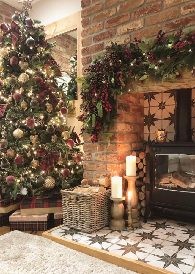 Cosy Christmas fireplace with glowing wood burner, festive garland, and a wicker log basket beside a decorated tree.