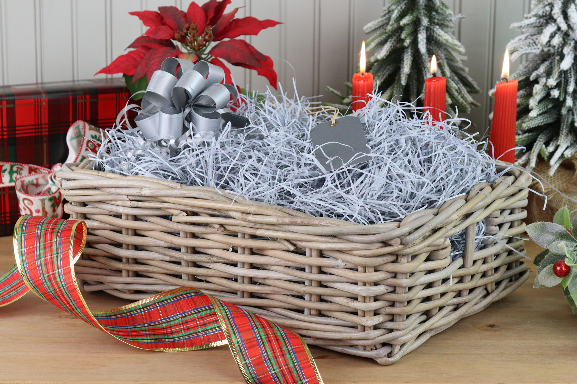 Grey wicker Christmas hamper with silver bow and shredded paper, ready to be filled with festive gifts and treats.