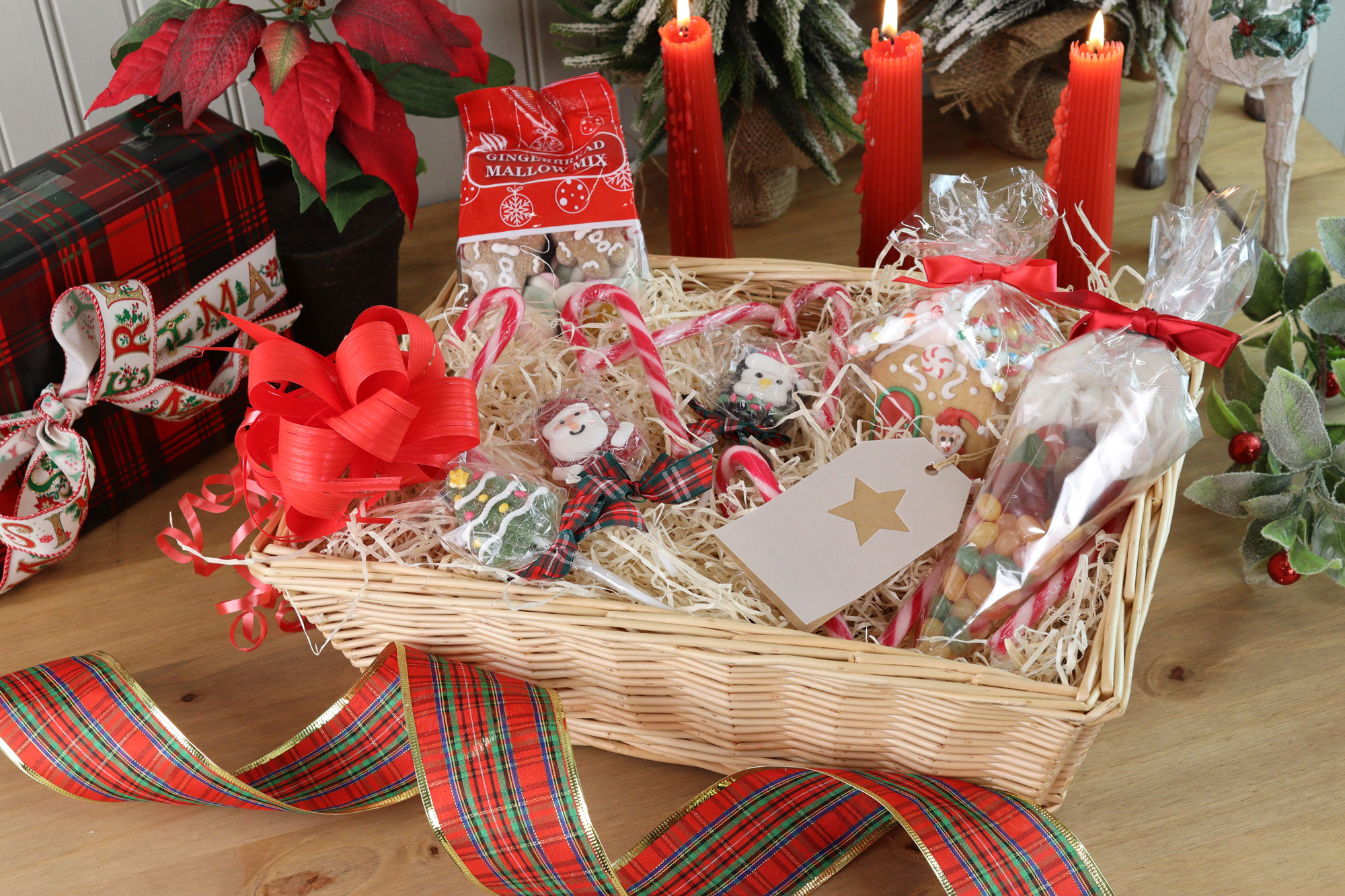 Christmas sweet hamper with gingerbread, candy canes, marshmallows and novelty lollies in a wicker tray with red ribbon.