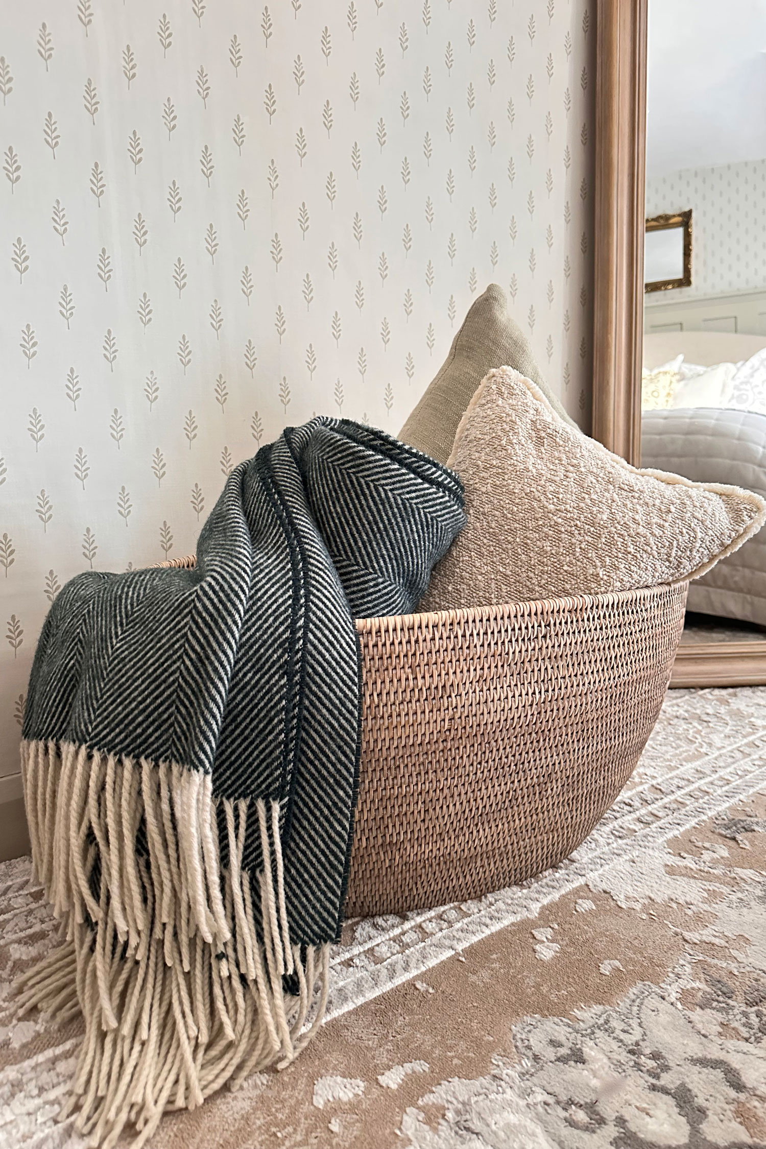 Neutral woven blanket basket used as cosy living room storage, filled with textured cushions and a soft herringbone throw.