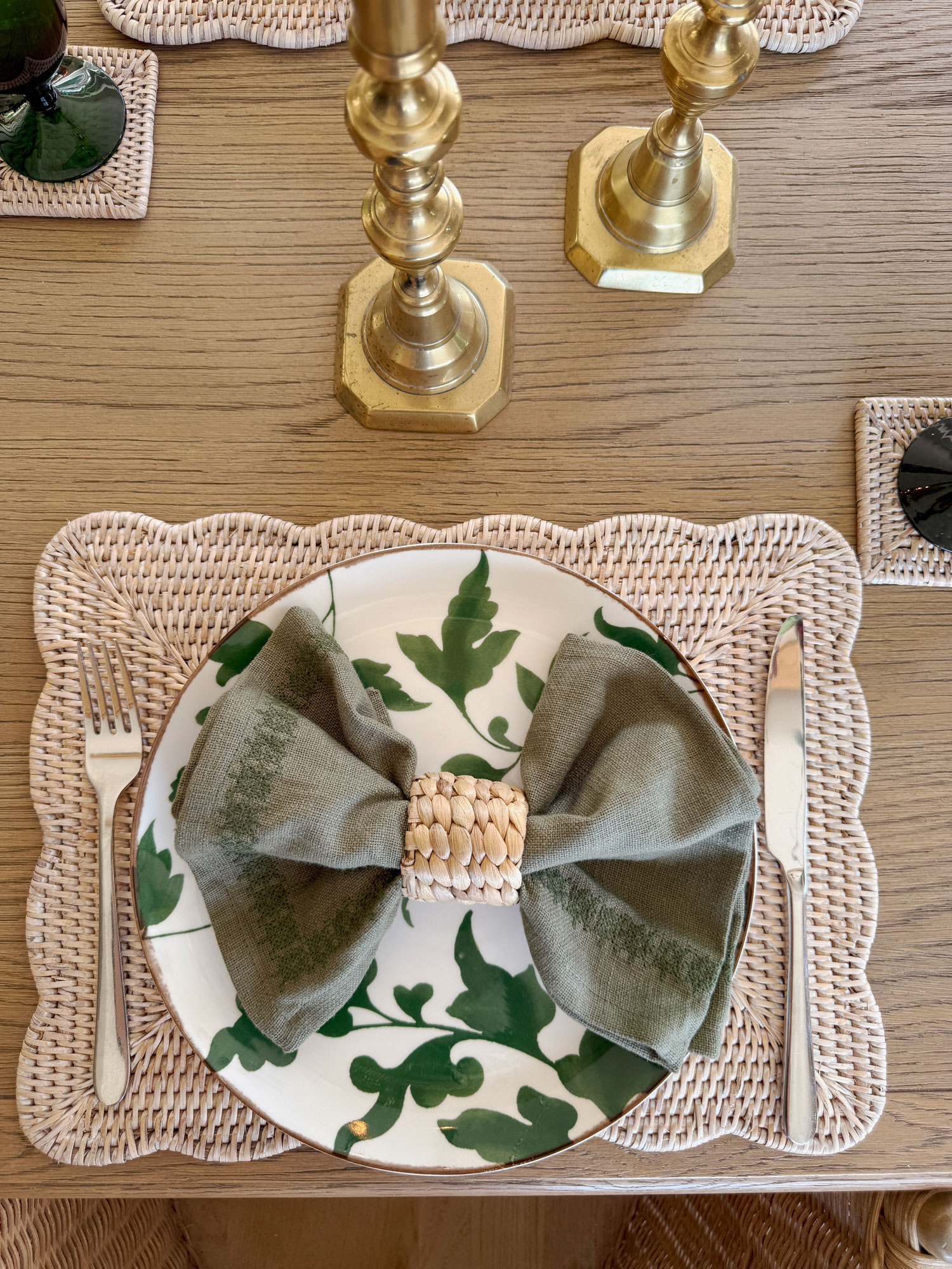 Beautiful place setting with scalloped wicker placemats and green leaf-patterned plates, finished with a knotted linen napkin ring.