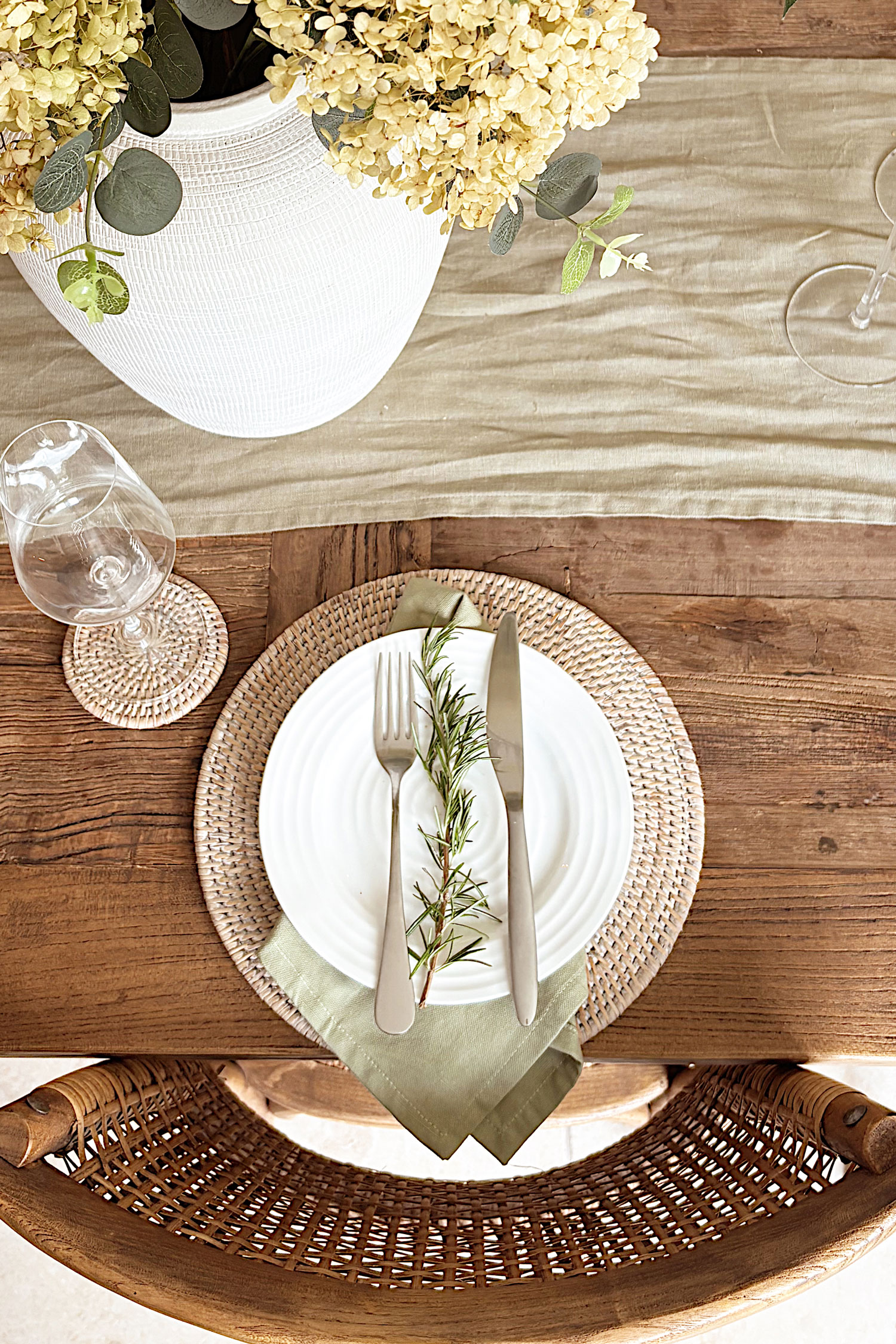 Round wicker placemat with layered green napkin and rosemary sprig, creating a simple and elegant natural table setting.