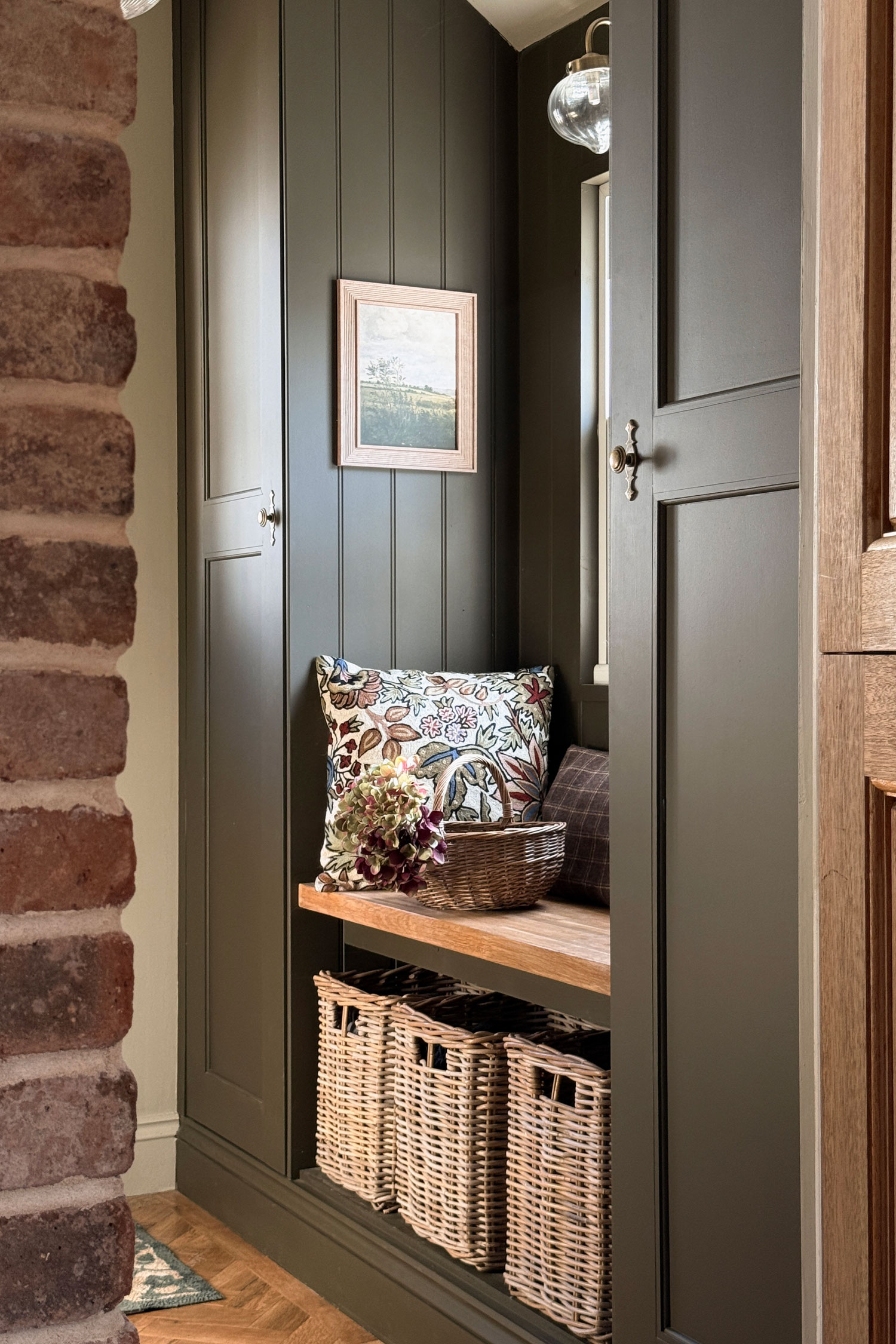 Cosy hallway nook with a floral cushion and rattan storage baskets under the bench, ideal for keeping shoes and accessories organised.