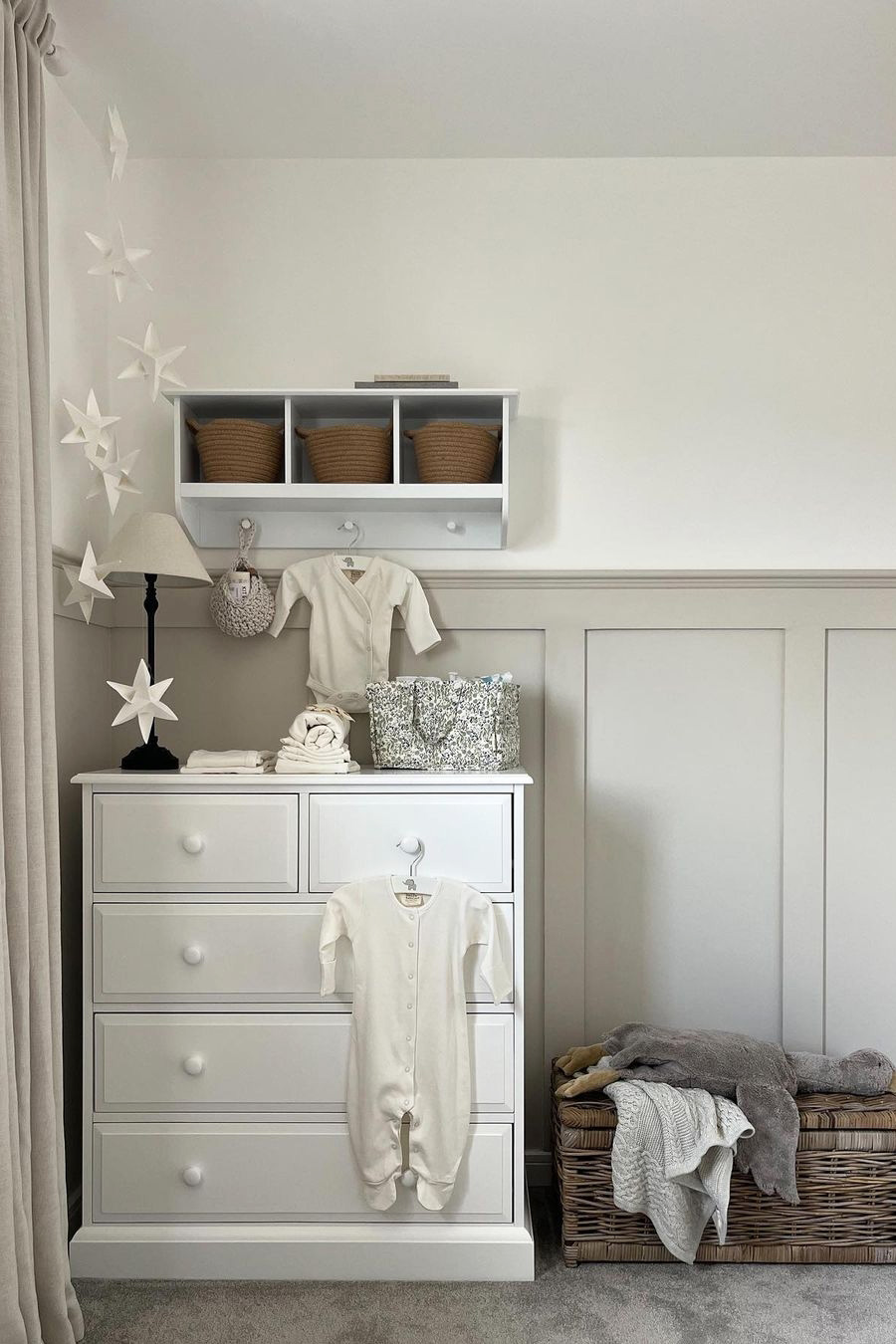Calm neutral nursery with a rattan toy basket tucked beside a white dresser, offering soft and practical toy storage.