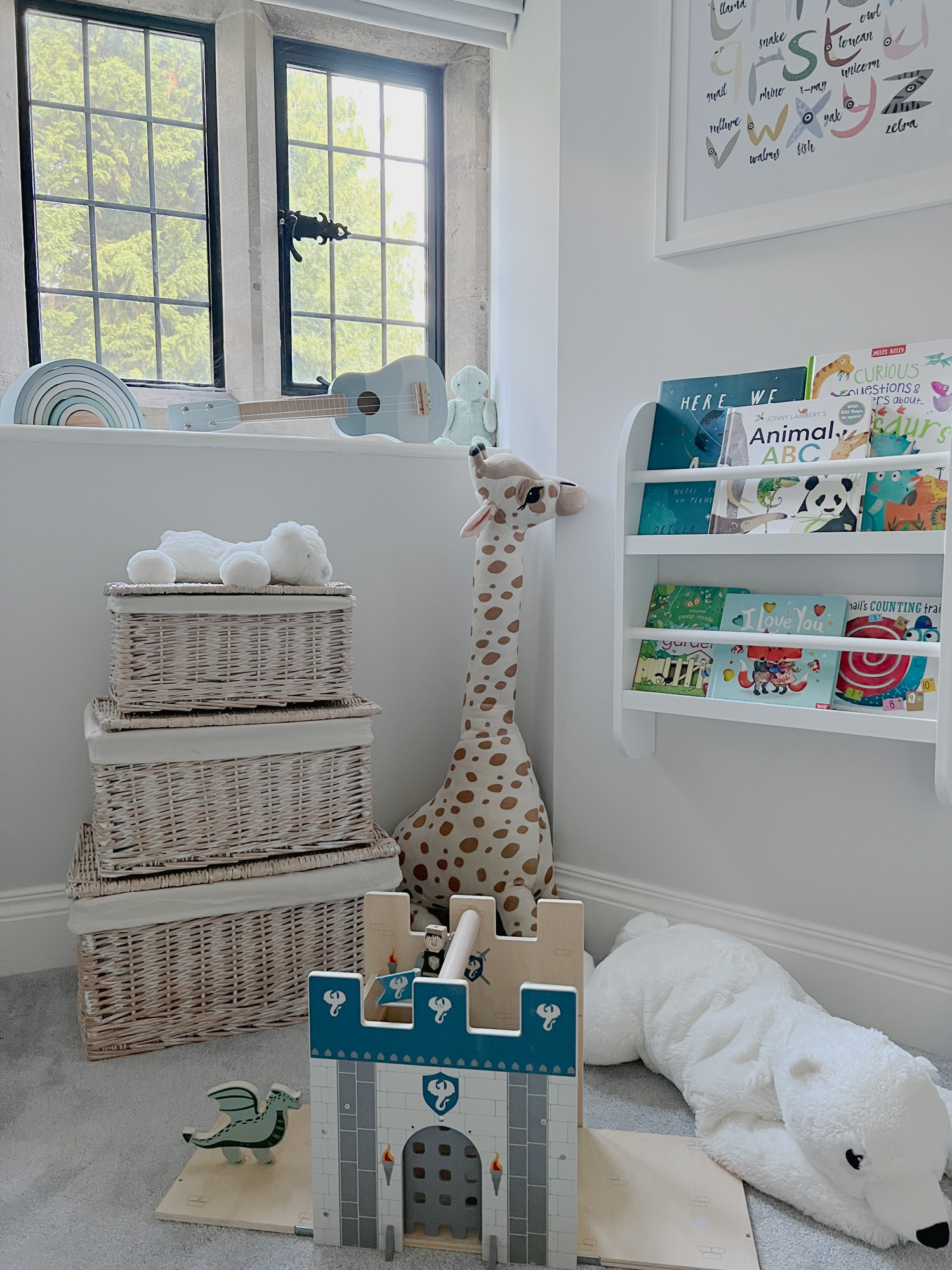 Bright playroom corner with stacked white storage baskets for nursery storage, styled beside a giraffe toy and front-facing book display.