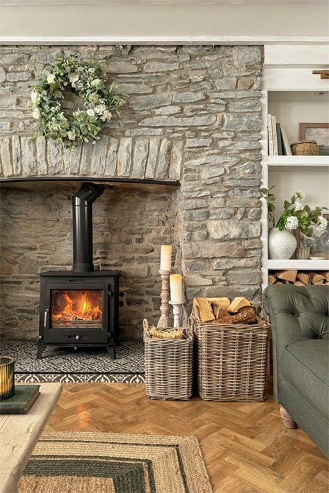 Cosy stone fireplace with wood-burning stove, wicker log baskets filled with firewood and rustic country décor