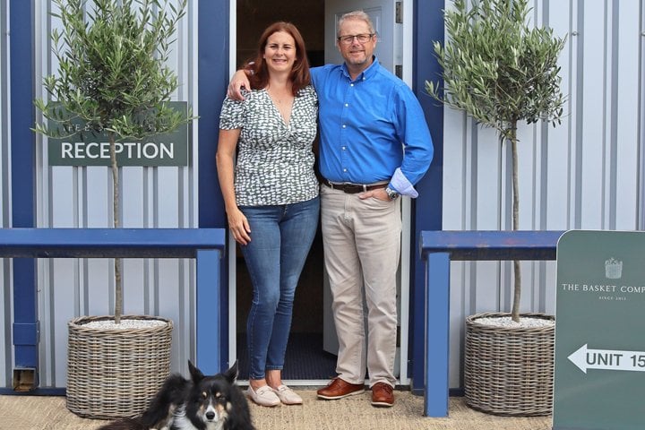 Catherine and Ian standing at The Basket Company reception entrance with dog in front and olive trees in wicker planters